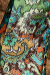 A close-up of a colorful paisley patterned fabric with swirling motifs in green, teal, orange, brown, beige, and white.