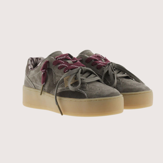 A low-top platform sneaker in dark gray suede and leather, featuring a thick beige gum sole, gray laces, and burgundy ribbon laces tied in a bow.
