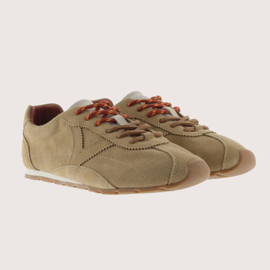 A pair of beige suede low-top sneakers with brown laces against a light beige background.