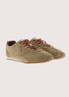 A pair of beige suede low-top sneakers with brown laces against a light beige background.