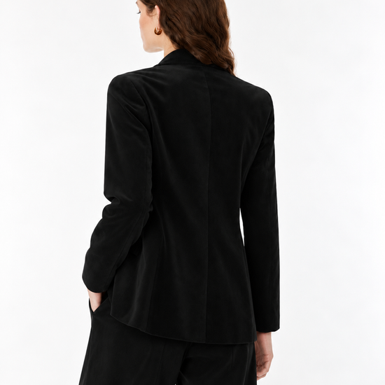 A woman shown from the back wearing a black long-sleeve blazer and matching black trousers against a plain white studio background.