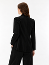 A woman shown from the back wearing a black long-sleeve blazer and matching black trousers against a plain white studio background.