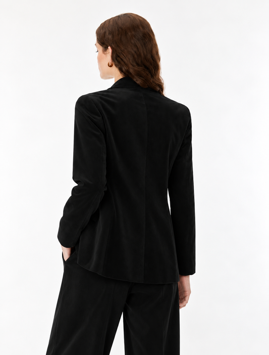 A woman shown from the back wearing a black long-sleeve blazer and matching black trousers against a plain white studio background.