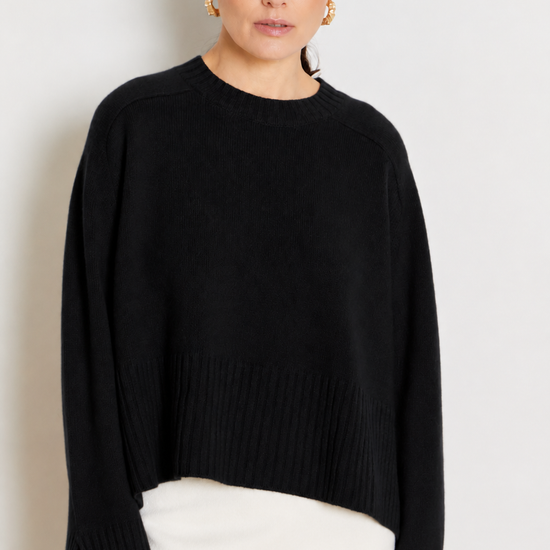 model wearing a black crew neck sweater and a white skirt on a plane background 