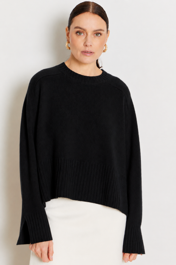 model wearing a black crew neck sweater and a white skirt on a plane background 