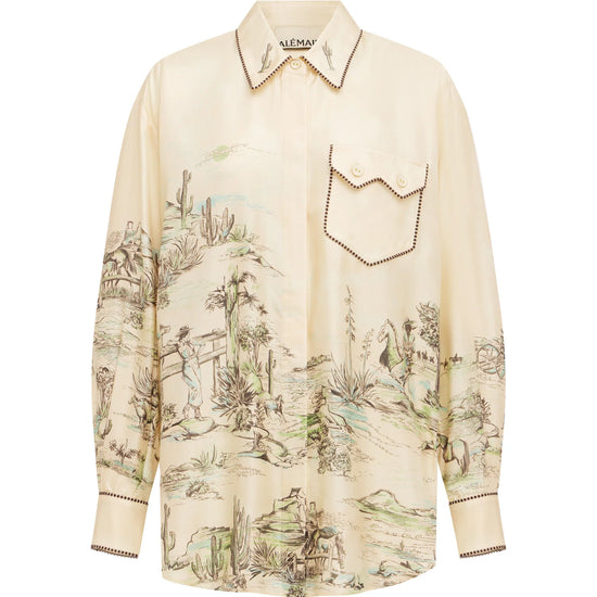 A cream-colored long-sleeve button-up shirt with a detailed scenic landscape print in muted green and brown tones, featuring a chest pocket with decorative stitching.