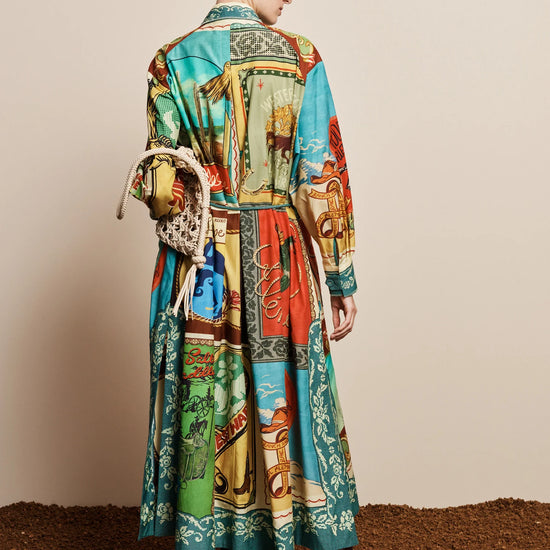 A model is shown from behind wearing a long-sleeved, belted midi dress with a vibrant multicolor patchwork print. The dress features a mix of turquoise, green, red, and yellow panels with a western-themed design.