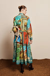 A model is shown from behind wearing a long-sleeved, belted midi dress with a vibrant multicolor patchwork print. The dress features a mix of turquoise, green, red, and yellow panels with a western-themed design.