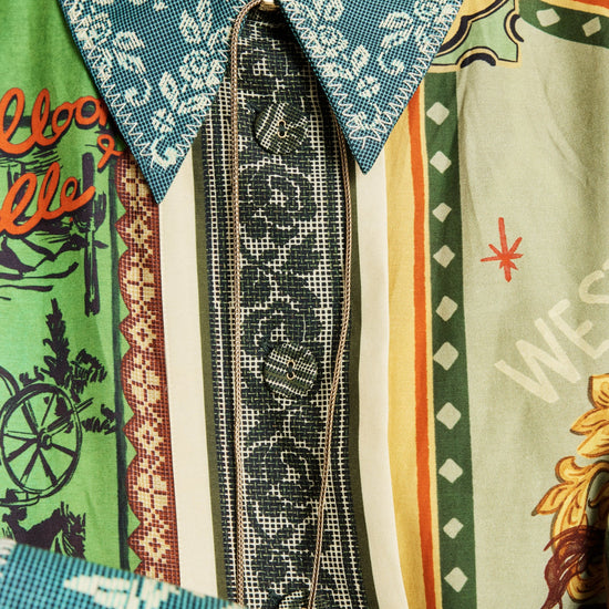 A close-up of a person wearing a highly patterned, multi-colored shirt with a teal paisley collar, a black patterned tie, and vertical panels of green, beige, orange, and white.