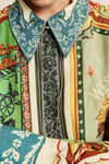 A close-up of a person wearing a highly patterned, multi-colored shirt with a teal paisley collar, a black patterned tie, and vertical panels of green, beige, orange, and white.