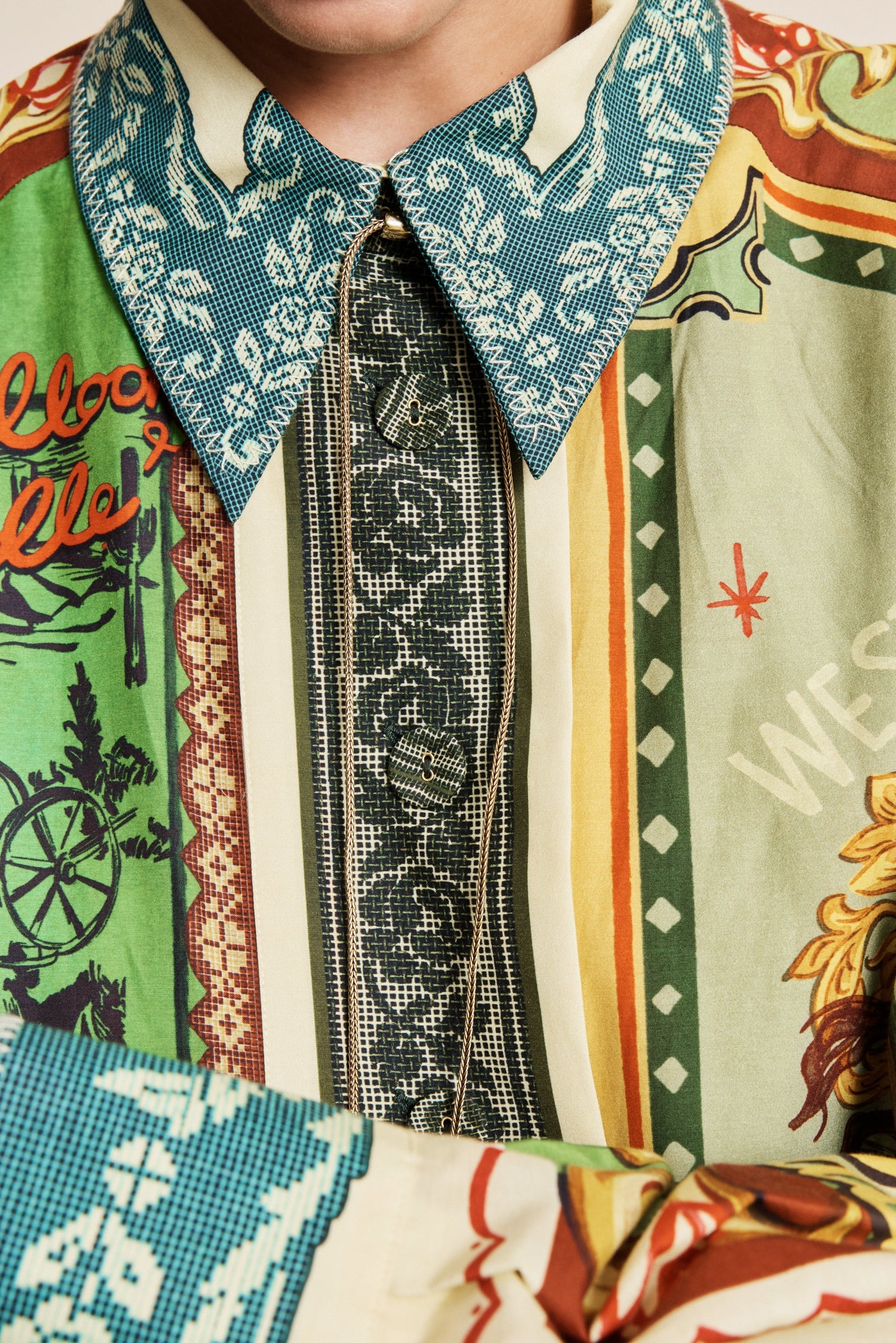 A close-up of a person wearing a highly patterned, multi-colored shirt with a teal paisley collar, a black patterned tie, and vertical panels of green, beige, orange, and white.