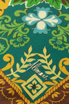 A close-up of a patterned scarf featuring a teal background with green, yellow, and light blue floral motifs, plus a brown decorative border at the bottom.