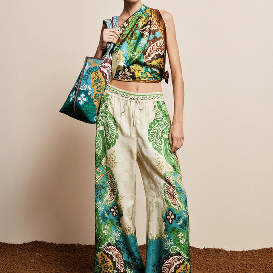 Model wearing a colorful outfit with a patterned top and pants, holding a matching handbag against a neutral background.