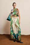 Model wearing a colorful outfit with a patterned top and pants, holding a matching handbag against a neutral background.
