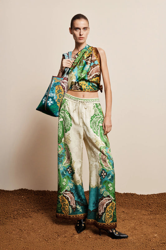 Model wearing a colorful outfit with a patterned top and pants, holding a matching handbag against a neutral background.