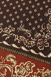 Close-up of a patterned scarf featuring a dark brown upper section with beige floral motifs and the script brand name  and a red lower section with beige ornamental paisley and border details.