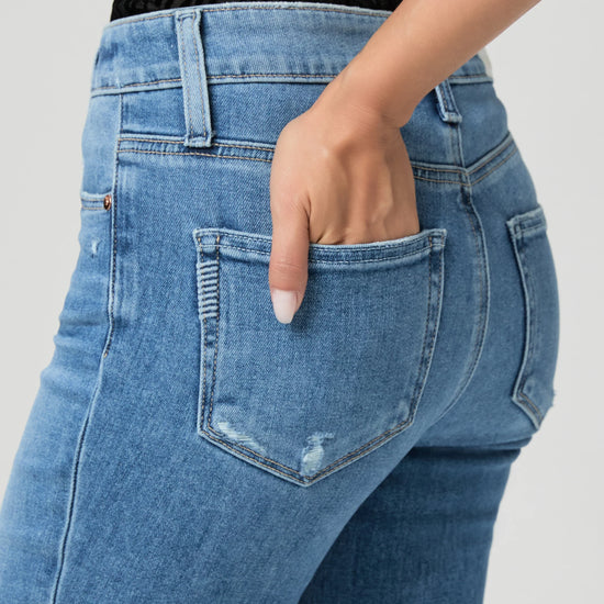 Blue jeans by Paige worn by a person on a white background close up