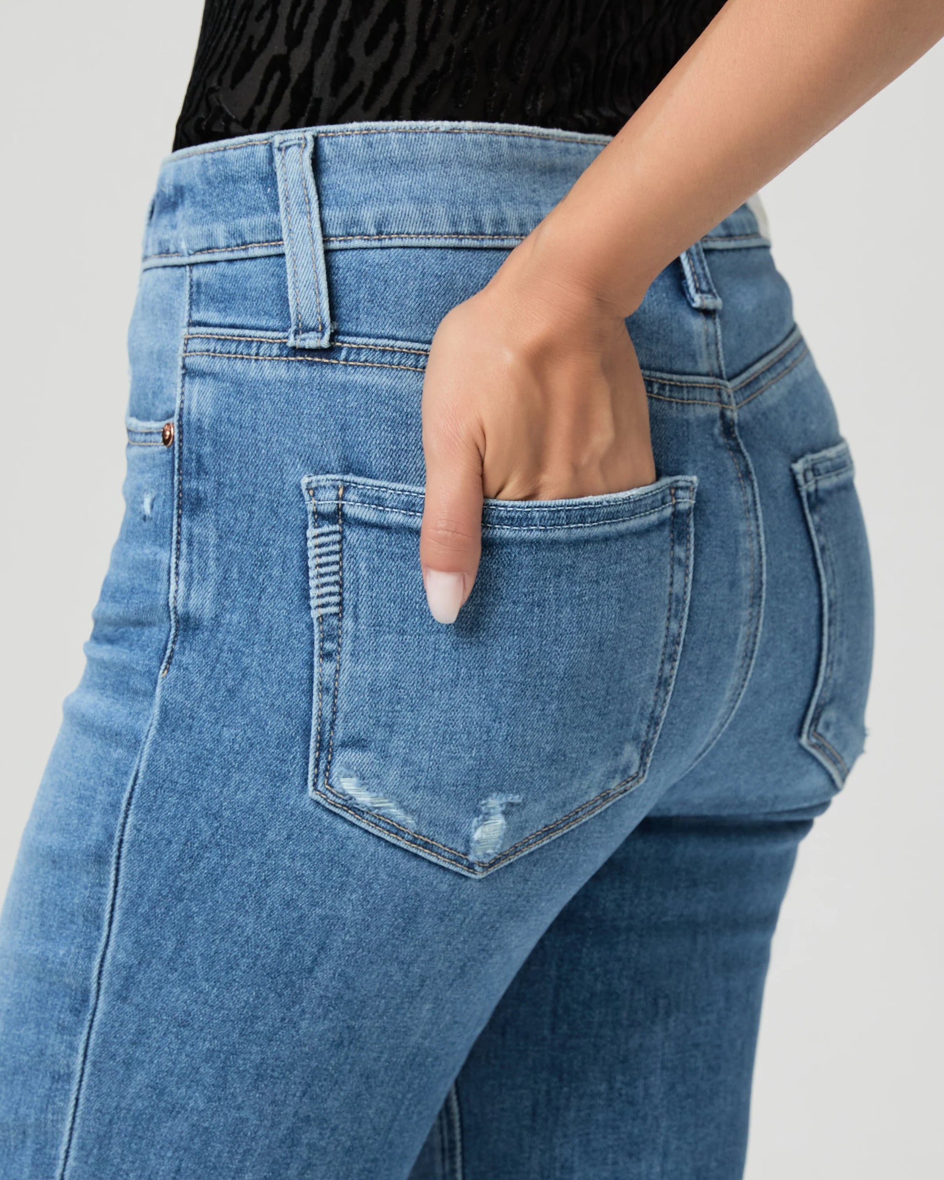 Blue jeans by Paige worn by a person on a white background close up