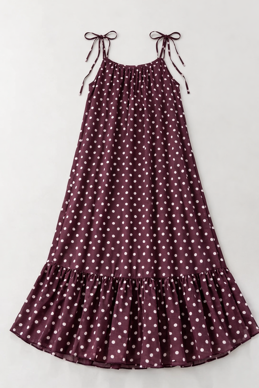 Plum coloured polka dot dress with thin straps on a light gray background
