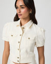 Woman wearing a white denim jacket with gold buttons on a plain background