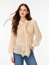 A woman wearing a light beige long-sleeve blouse with a ruffled front placket and collar, paired with blue jeans, photographed against a plain white studio background.