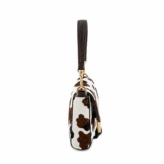 A small wristlet clutch with a brown and white cow print pattern, a dark brown wrist strap, and gold-tone hardware, shown against a plain white background.