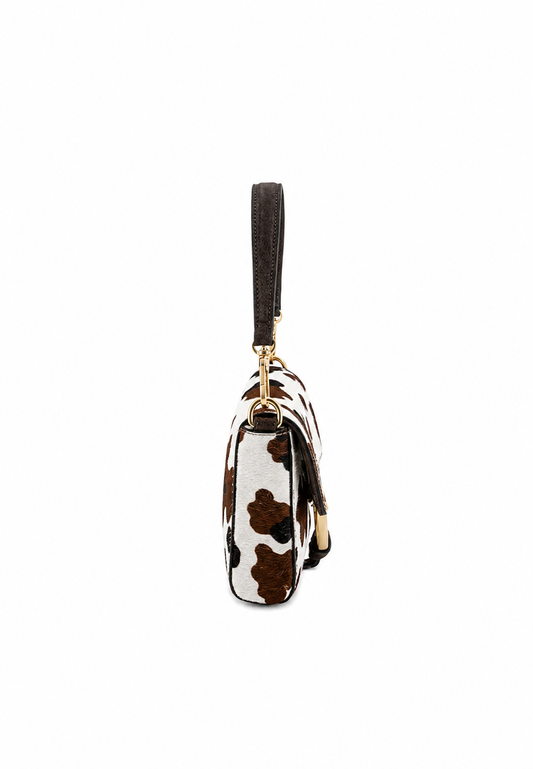 A small wristlet clutch with a brown and white cow print pattern, a dark brown wrist strap, and gold-tone hardware, shown against a plain white background.