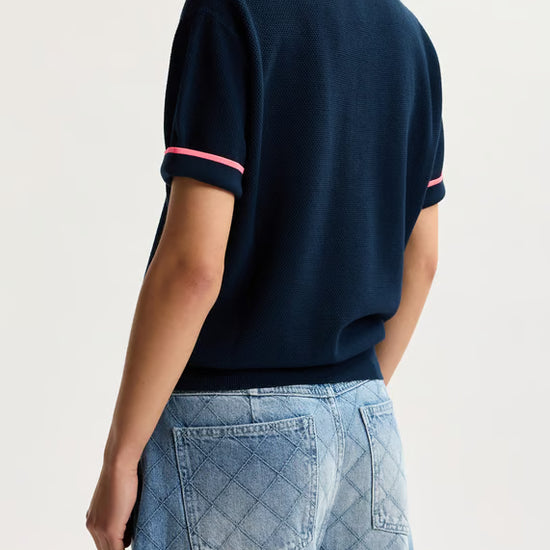 Person wearing a navy blue polo shirt with pink accents and blue jeans on a light background