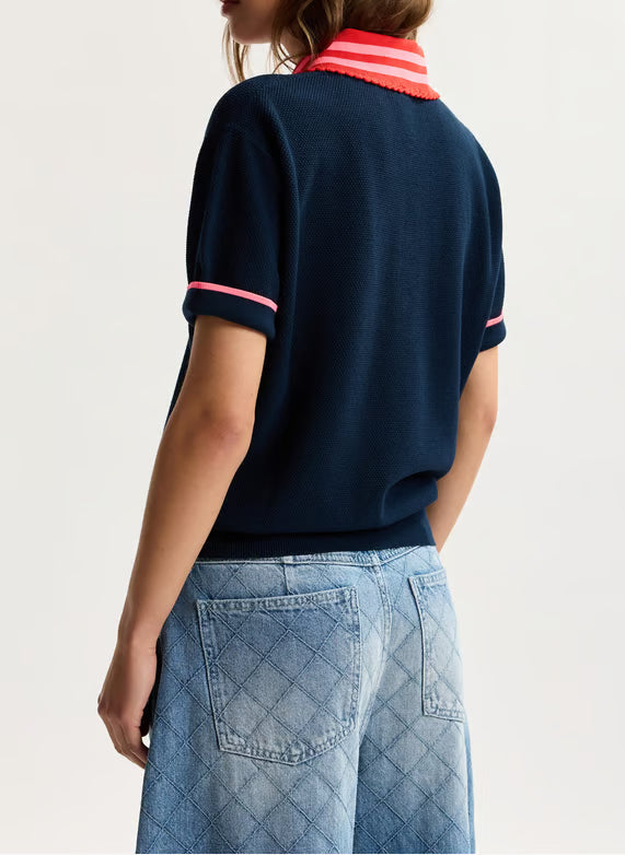 Person wearing a navy blue polo shirt with pink accents and blue jeans on a light background