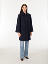 A woman modeling a dark navy blue wool-blend coat with front buttons, paired with light blue jeans and brown shoes, standing against a plain white studio background.
