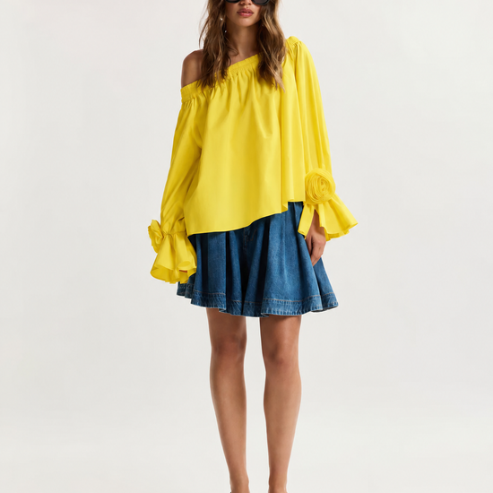 Woman wearing a yellow off-shoulder top and blue denim skirt on a white background