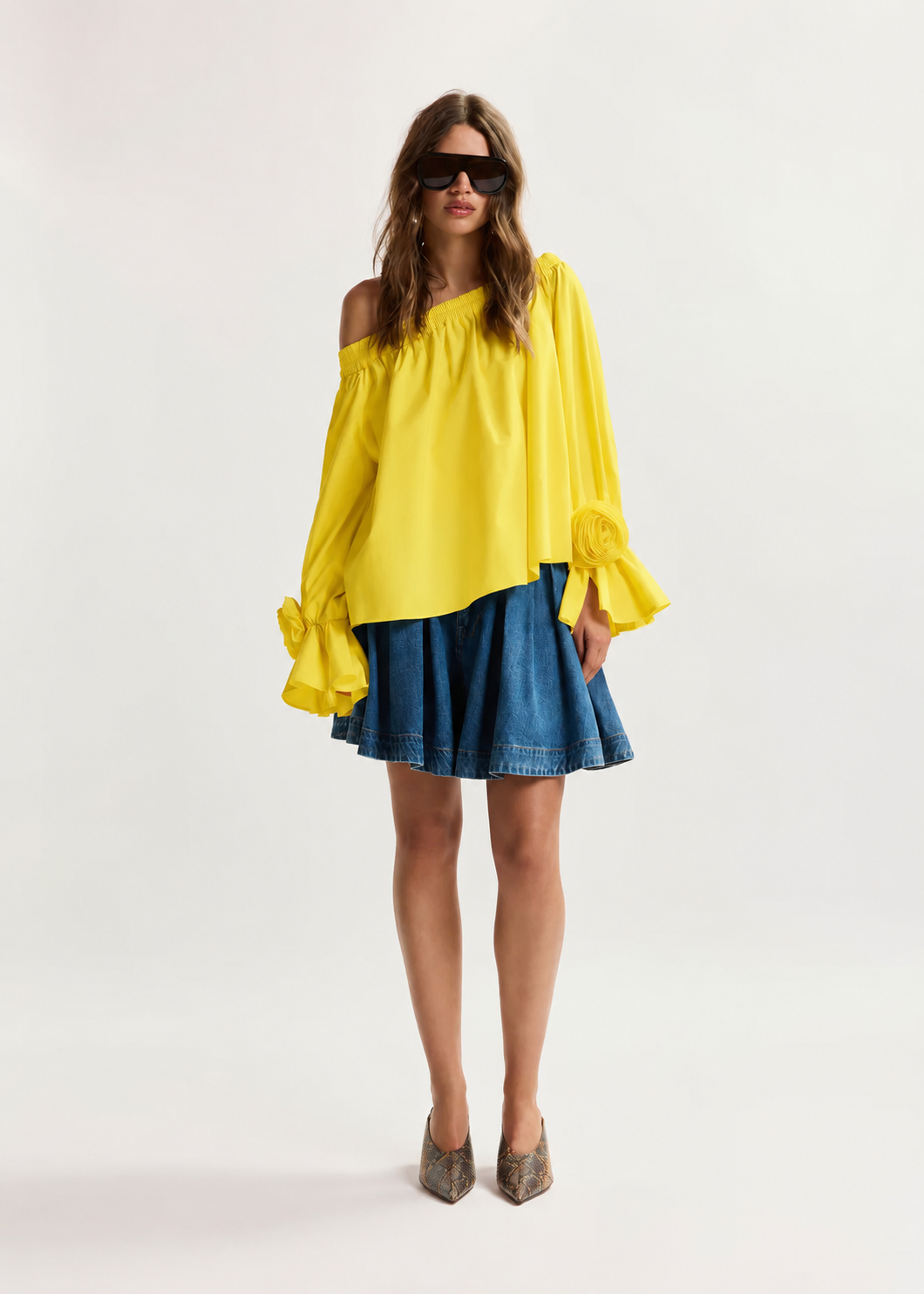 Woman wearing a yellow off-shoulder top and blue denim skirt on a white background