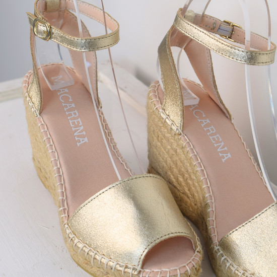 A gold wedge sandal with open toes and an ankle strap 