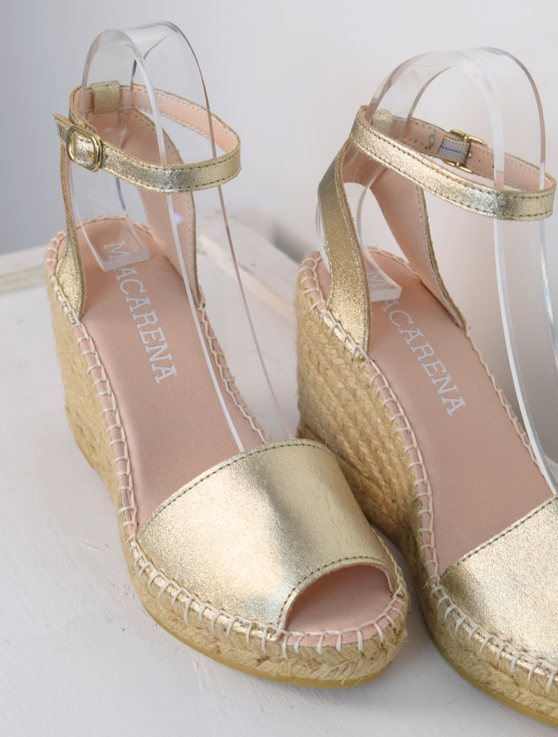 A gold wedge sandal with open toes and an ankle strap 