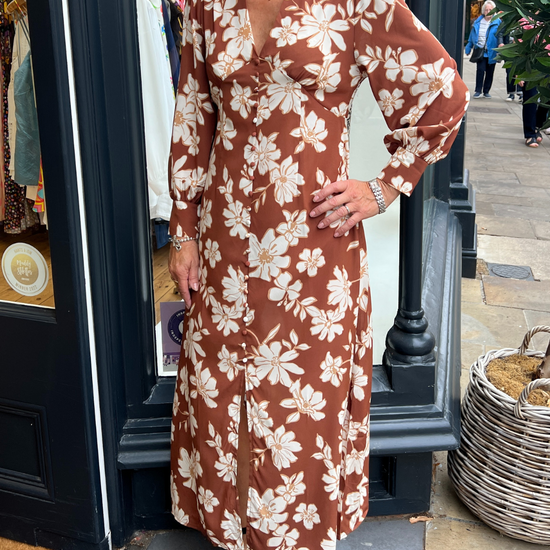 A long vintage style dress with a tan background and a white floral print 