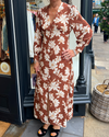 A long vintage style dress with a tan background and a white floral print 
