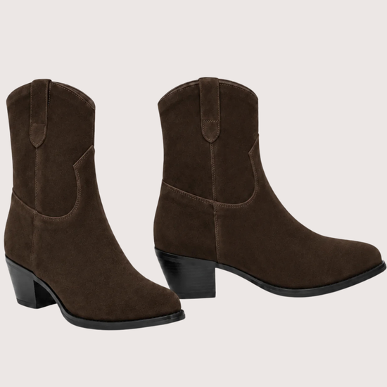 A pair of dark brown suede western-style ankle boots with low block heels, shown from the side and back-three-quarter angles against a solid light beige background.
