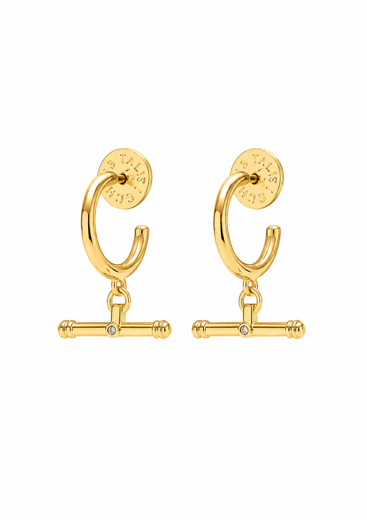 A pair of gold huggie hoop earrings with a dangling barbell charm and a small clear rhinestone in the center, shown on a plain white background.