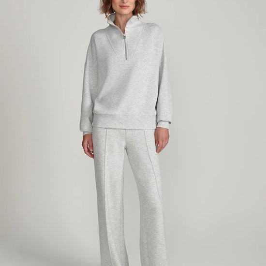A woman modeling a light gray heathered loungewear set consisting of a quarter-zip long-sleeve top and matching wide-leg sweatpants, photographed against a neutral light gray studio background.