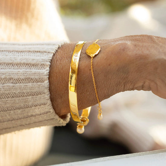 Gold bracelets on a wrist with a blurred natural background
