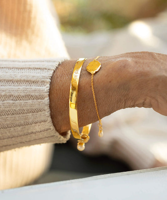Gold bracelets on a wrist with a blurred natural background
