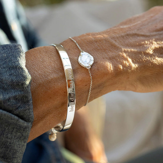 Close-up of a person's wrist wearing two bracelets with engraved text, blurred background