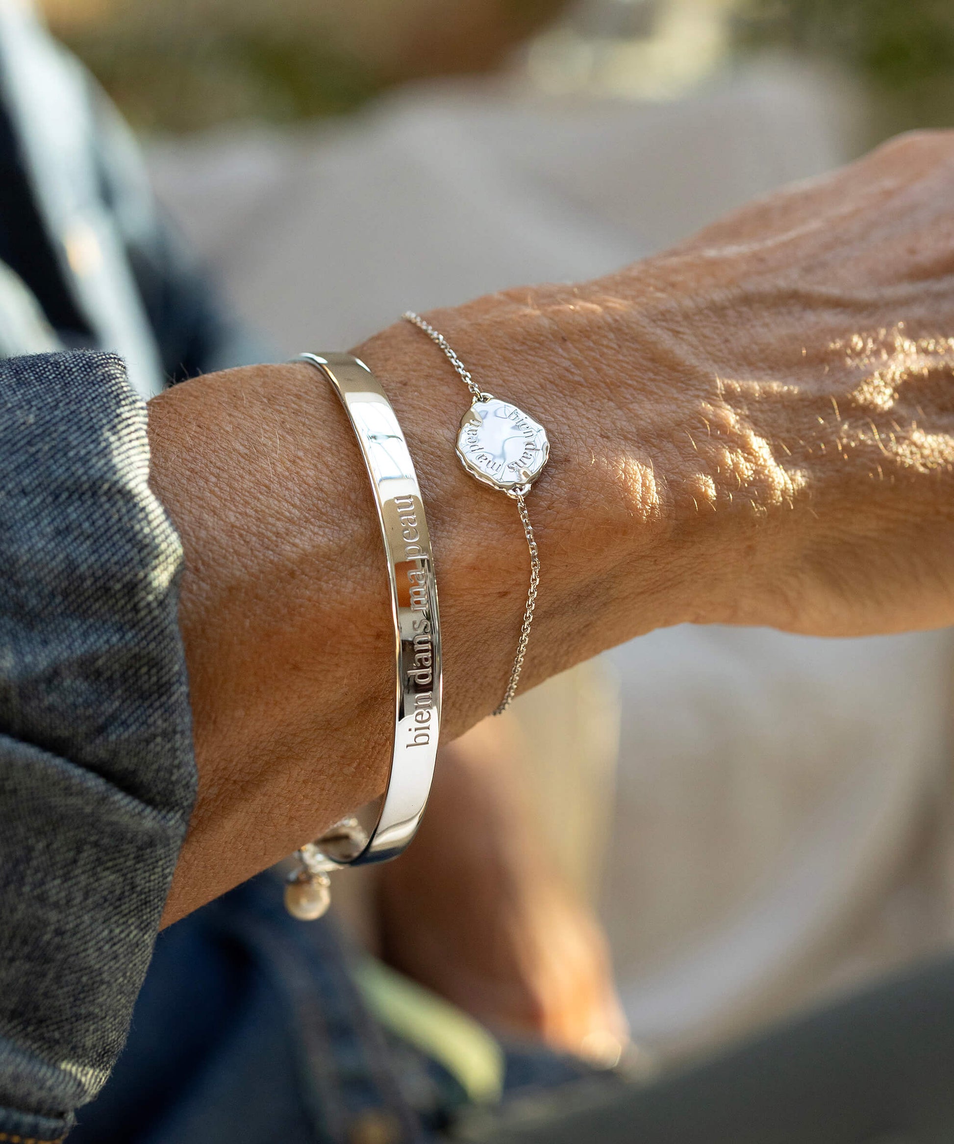 Close-up of a person's wrist wearing two bracelets with engraved text, blurred background