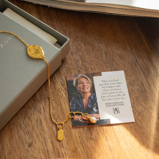 Gold necklace with a pendant on a card featuring a woman's face, placed on a wooden surface.