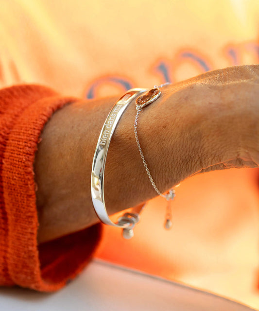Silver bracelet on a wrist with an orange sleeve against a blurred background