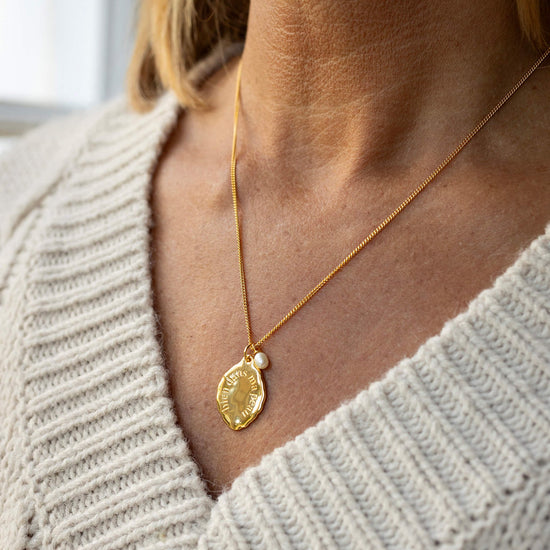 Gold necklace with a pendant worn by a person in a light gray sweater.