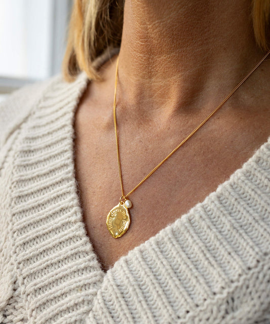 Gold necklace with a pendant worn by a person in a light gray sweater.