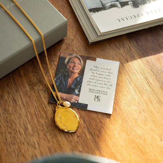Gold necklace with a pendant on a wooden surface next to a card and book.