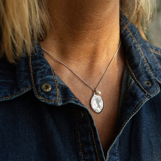 Person wearing a necklace with a pendant, visible under a denim shirt.