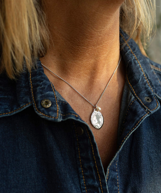 Person wearing a necklace with a pendant, visible under a denim shirt.